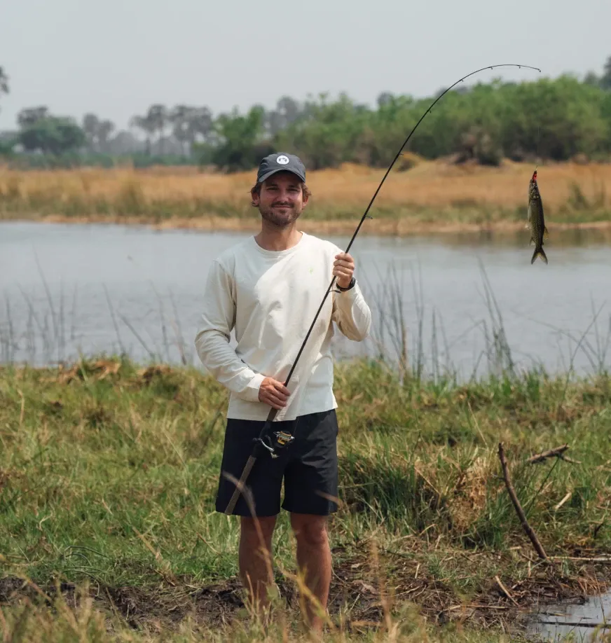 Guest fishing at the Okavango Delta near Daunara Safari Camp, standing by the water with a fishing rod and a freshly caught fish.