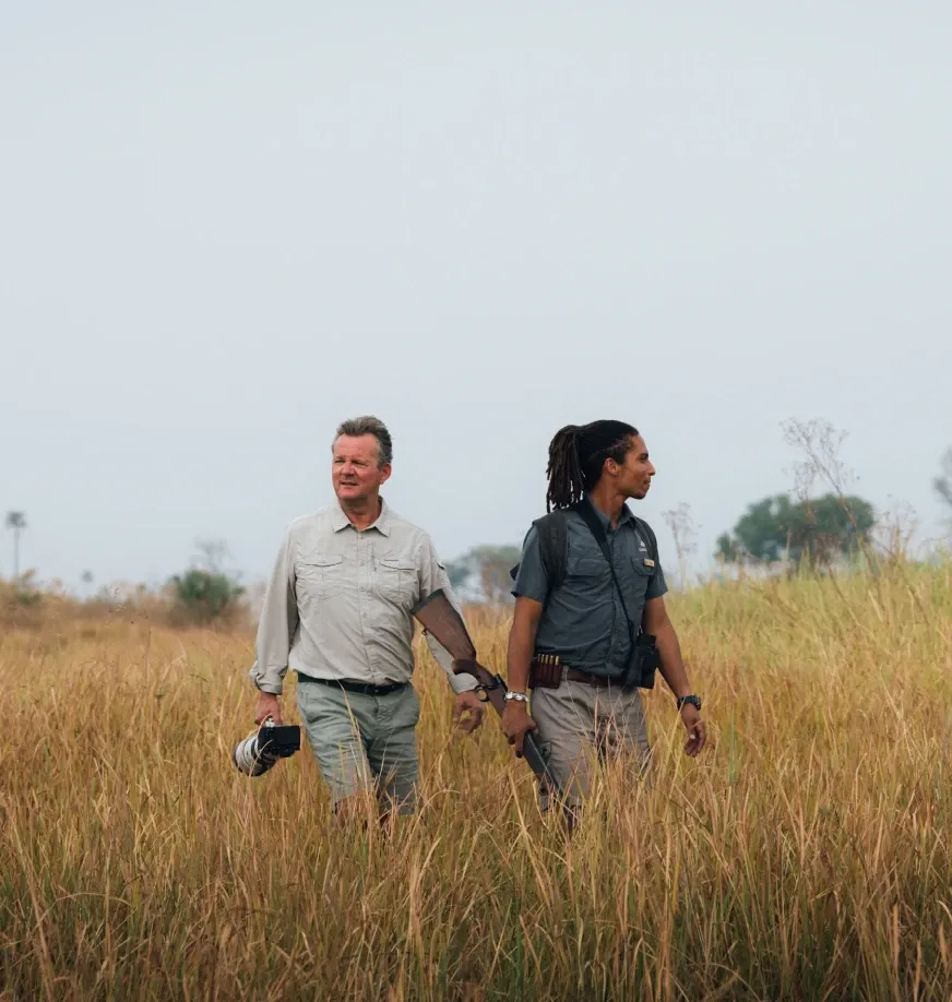 Guest on a walking safari in the Okavango Delta with a guide from Daunara Safari Camp, holding a camera to photograph wildlife.